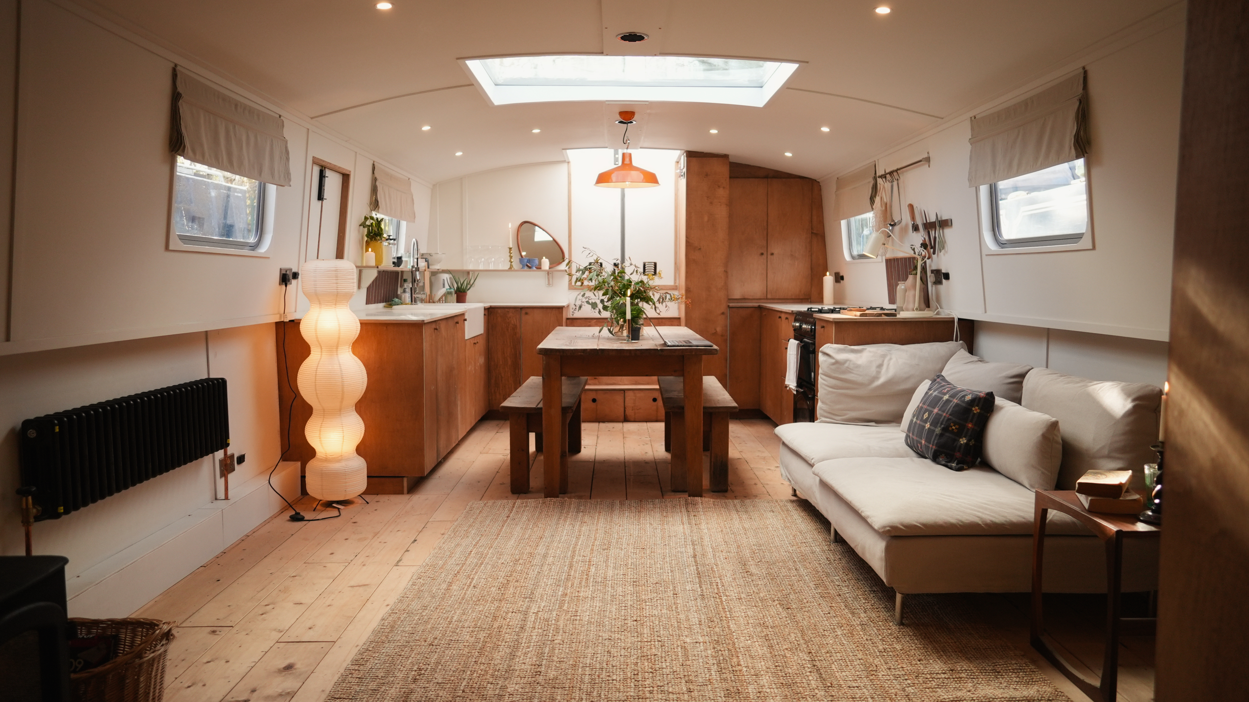 The interior of Rosanna Irwin's barge, showing a modern living area with wooden floors, a dining table, kitchen, and sofa.