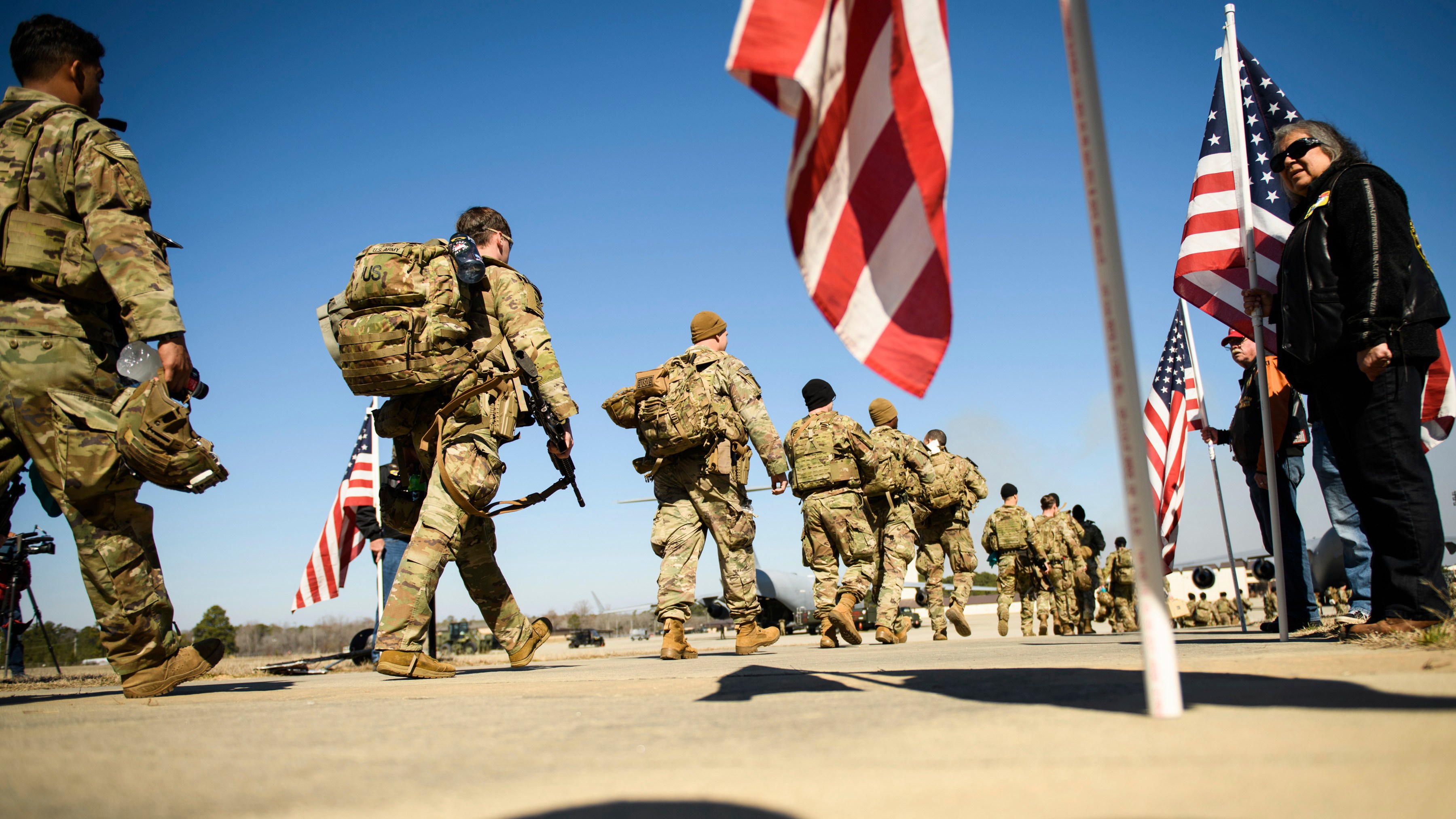 Paratroopers from Fort Bragg's 82nd Airborne Division walk towards a plane with US flags flying in the foreground.