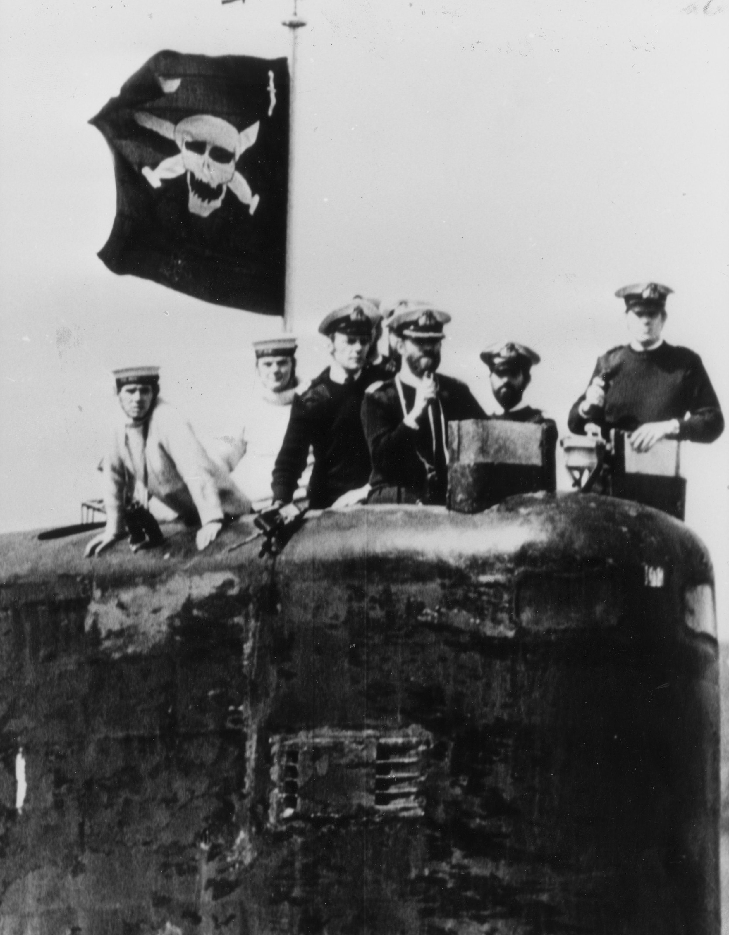 Captain Christopher Wreford-Brown and crew members on the tower of HMS Conqueror with a skull flag flying, signifying a successful mission in the Falklands War.