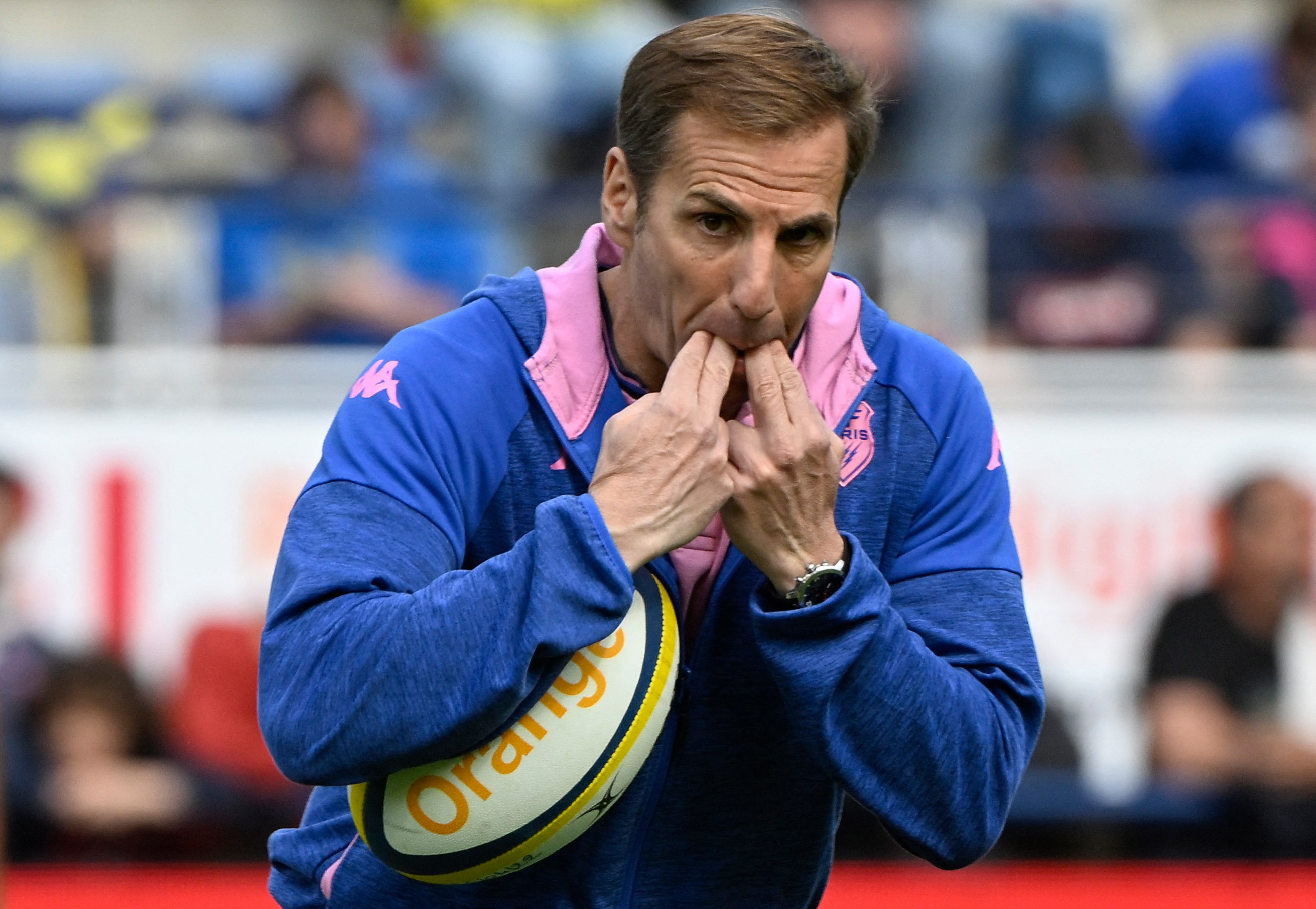 Stade Francais coach Gonzalo Quesada whistles with his fingers while holding a rugby ball during a match.