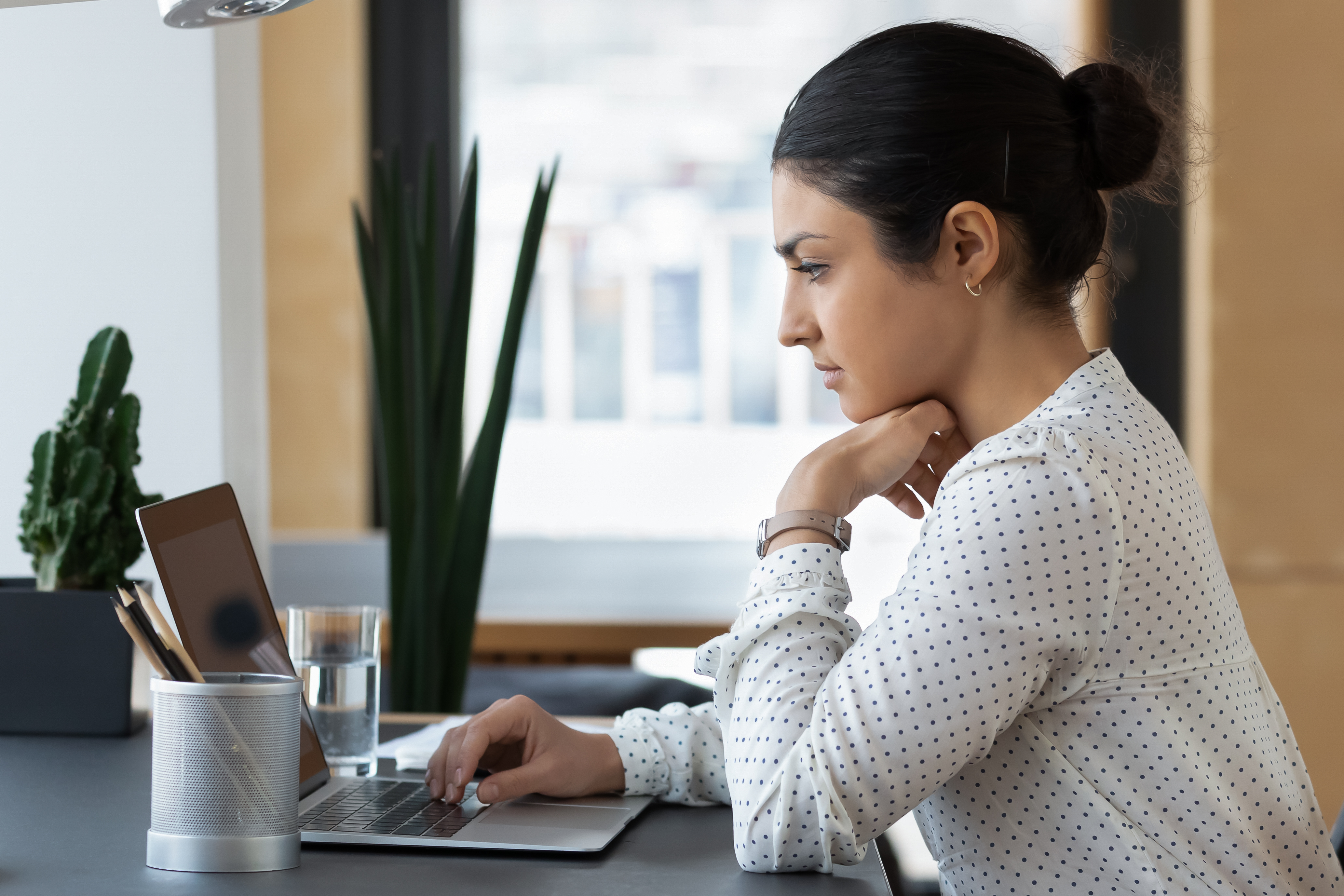 Pensive Indian woman looking at a laptop screen while working in an office.