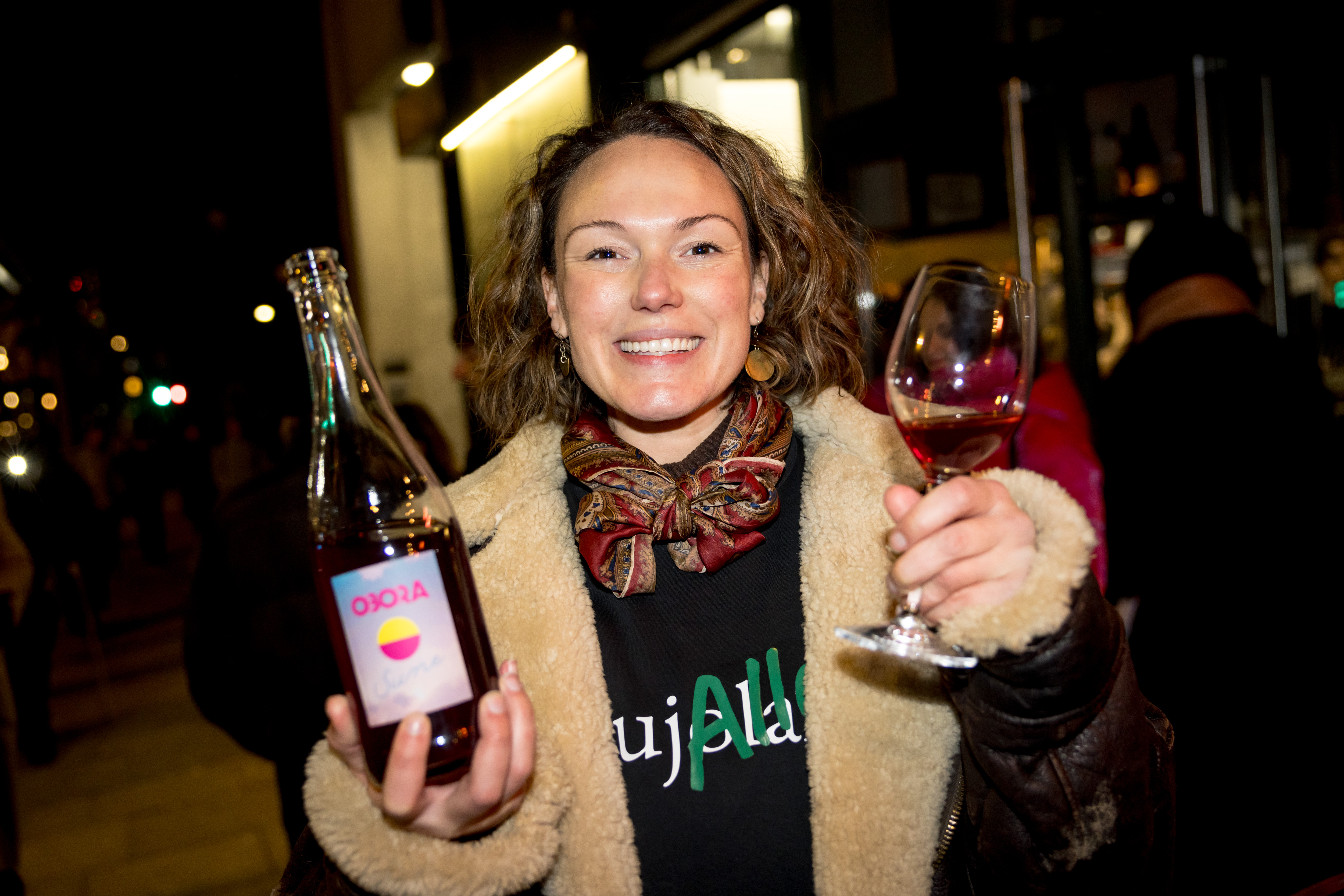 Restaurant owner Honey Spencer smiling while holding a bottle of Obora Sune and a glass of wine.