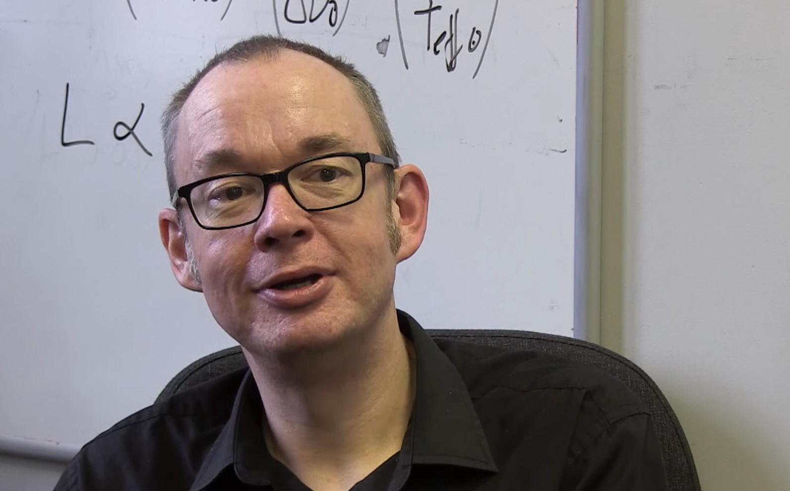 University of Birmingham Professor of Astrophysics Bill Chaplin wearing glasses, in front of a whiteboard with scientific equations.