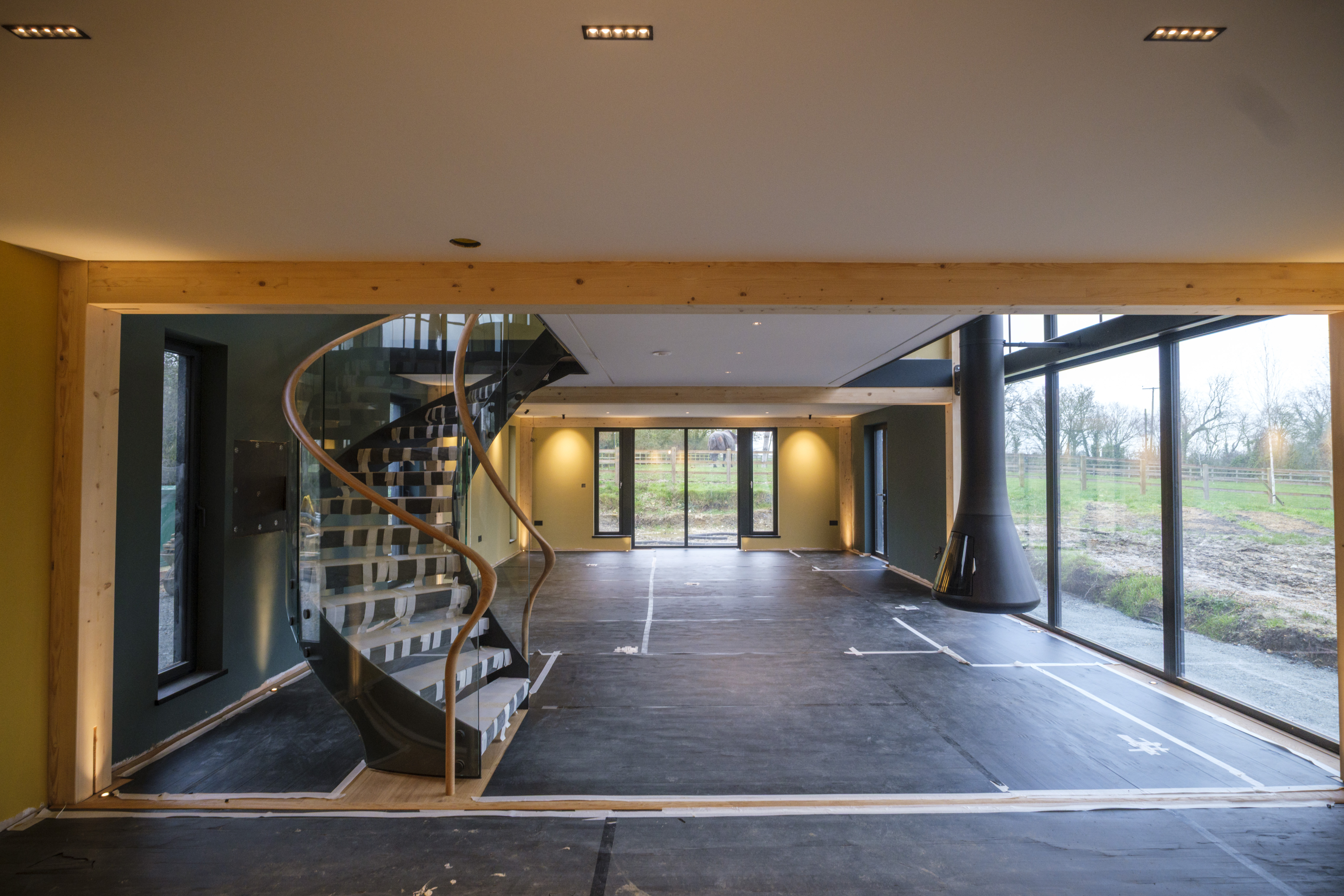 An unfinished living area with a spiral staircase, suspended fireplace, and floor-to-ceiling windows.