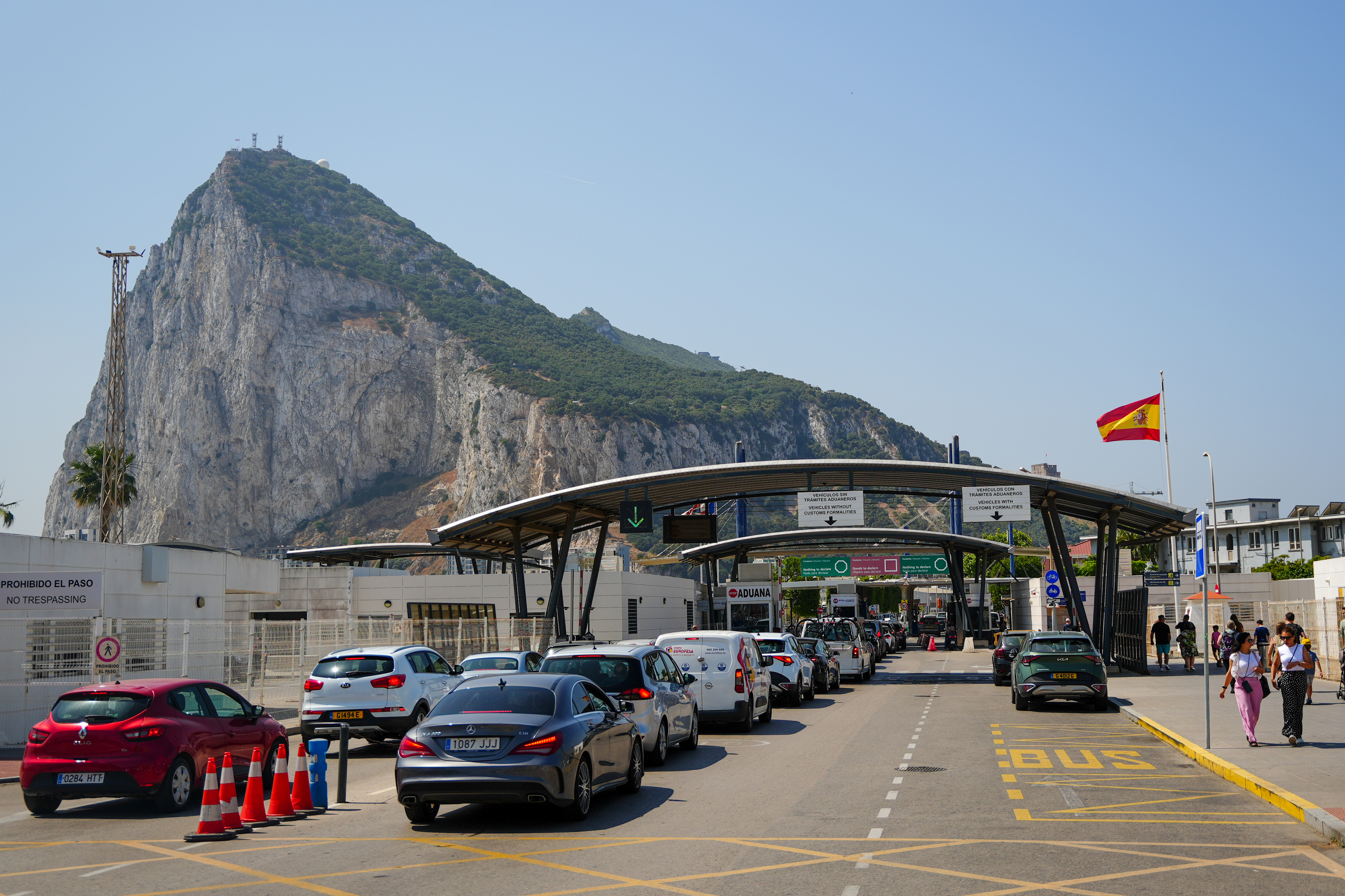 The border between Spain and the Rock of Gibraltar with cars queued for customs and pedestrians walking along the road, under a clear sky.