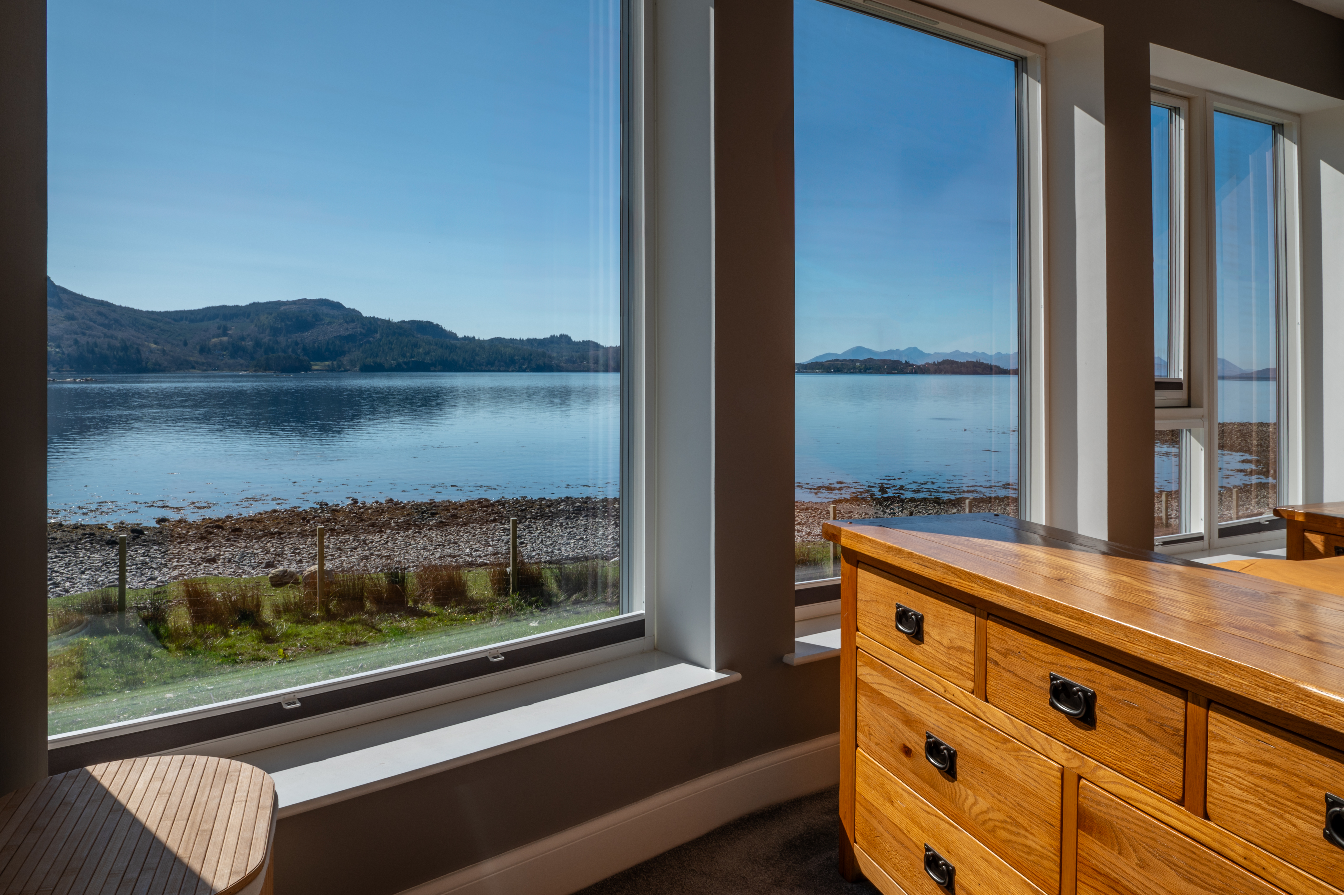 A scenic view of Loch Carron through multiple windows, with a wooden dresser in the foreground.