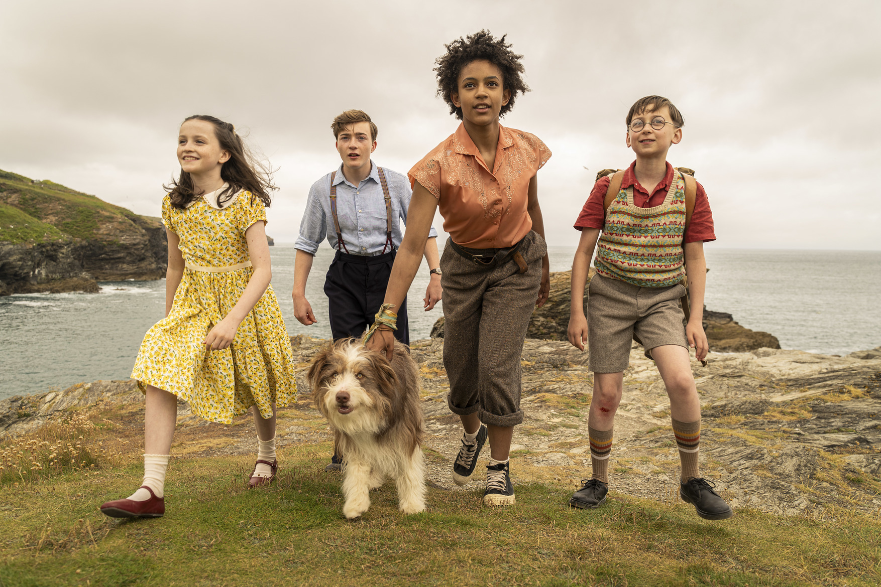 The Famous Five and their dog walking on a rocky coastline.