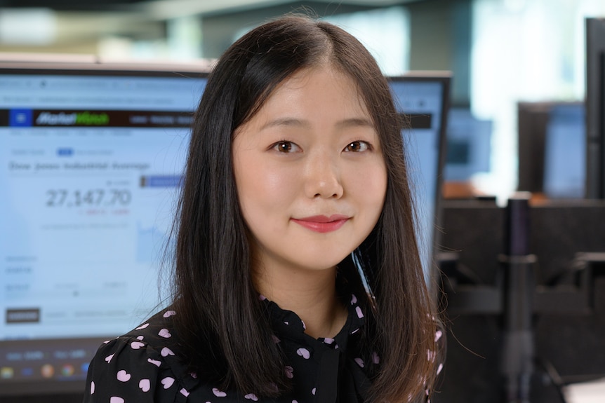 Younger woman with black hair sitting at office chair smiles in well lit office enviroment.