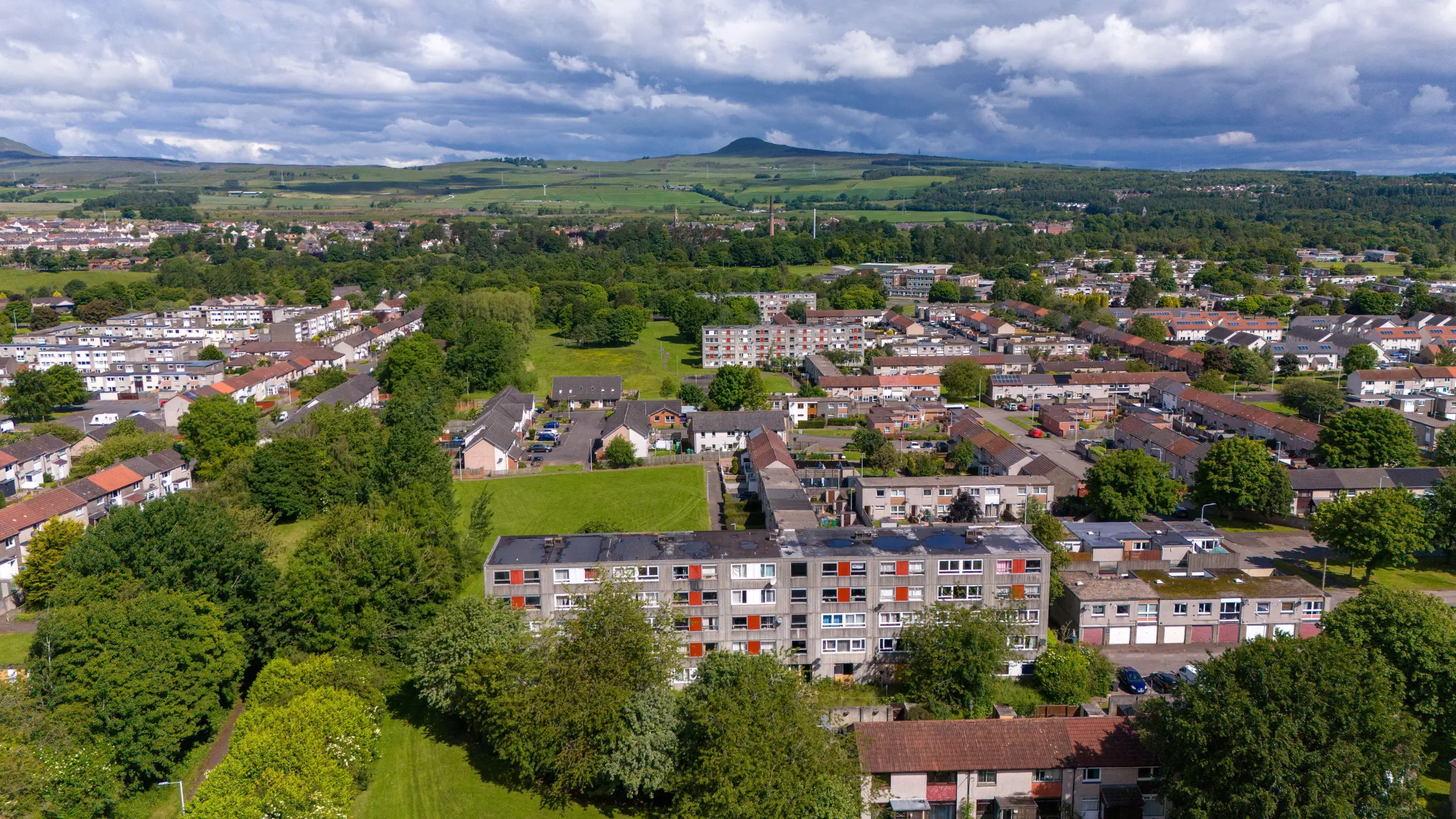 Aerial view of council housing at Keith Court, Glenrothes, with residential areas, green spaces, and distant hills under a cloudy sky.