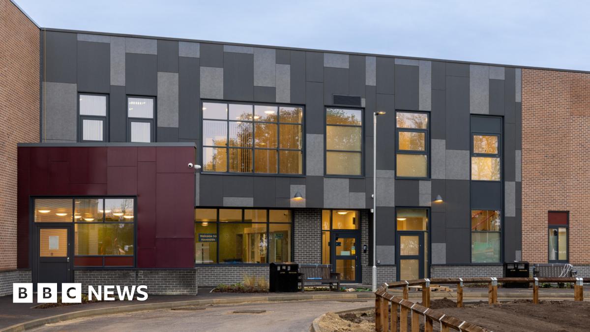 The exterior of the new mental health ward at Pilgrim Hospital in Boston. It is a multi-coloured building with large windows. It has a road in front of it and a muddy area surrounded by short wooden fencing.