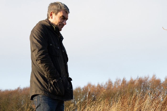 Cain stands over Zak's grave in a field in a scene from Emmerdale