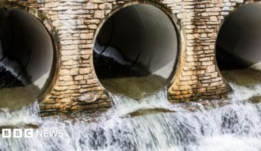 Water flows out of three openings of underground pipes. The pipes are surrounded by lightly coloured brickwork.