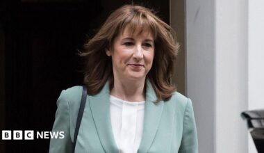 Rachel Reeves walks out of Number 10 Downing Street wearing a white blouse and light blue jacket smiling slightly with her mouth closed