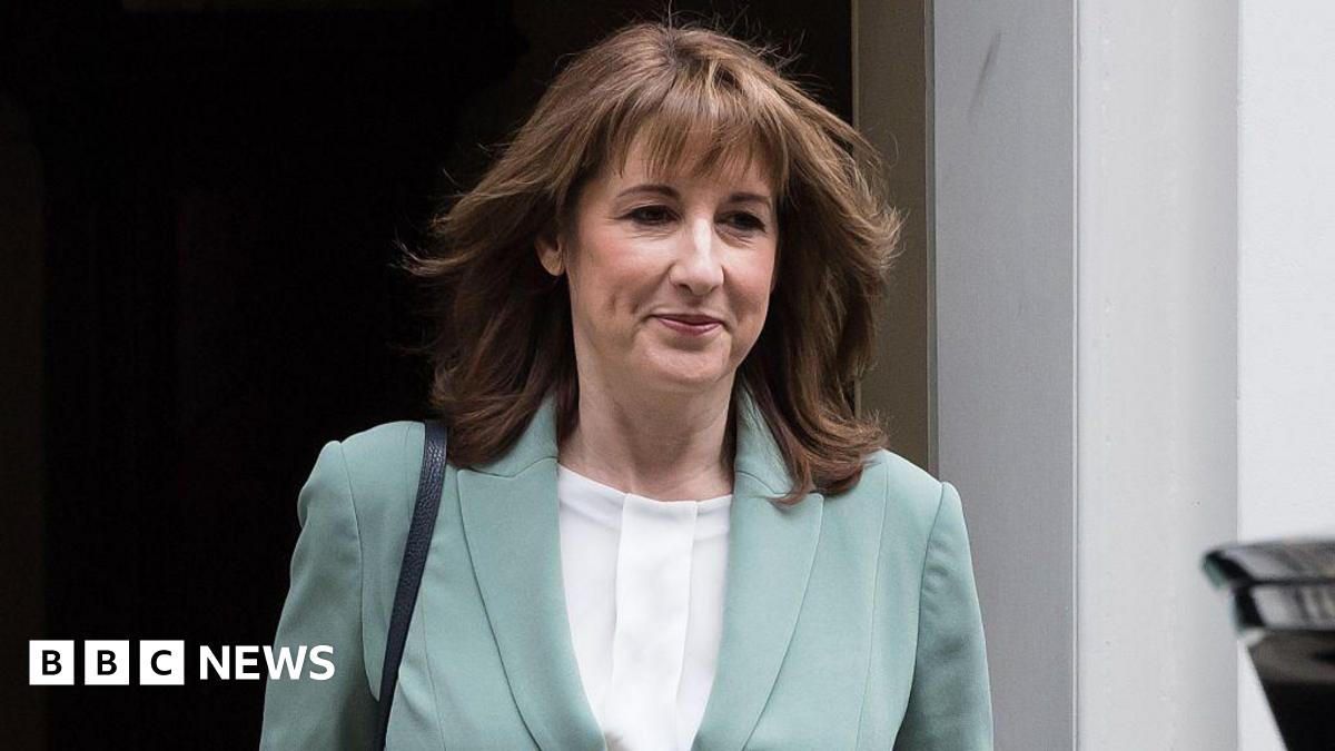Rachel Reeves walks out of Number 10 Downing Street wearing a white blouse and light blue jacket smiling slightly with her mouth closed