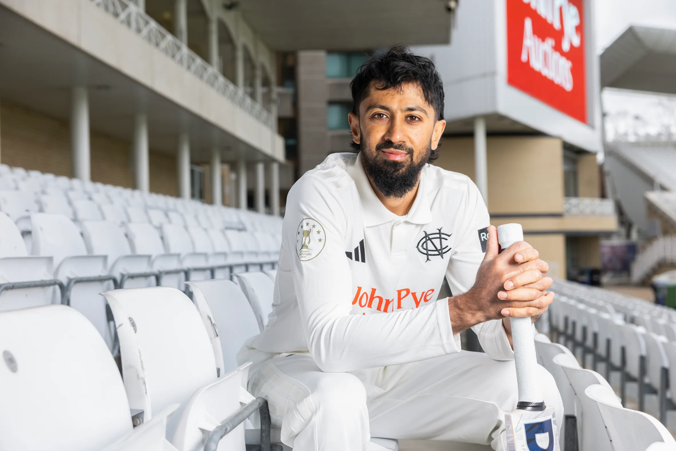 Nottinghamshire County cricketer Haseem Hameed sitting in the stands at Trent Bridge, holding a bat.
