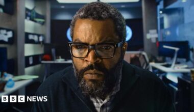 Ice Cube in an office facing the camera and staring intently at a screen