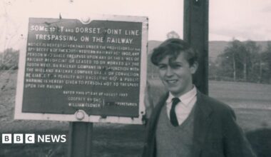 Black and white photo of Paul Antell as a teenager standing next to a sign which explains it is forbidden to trespass on the Somerset and Dorset line.