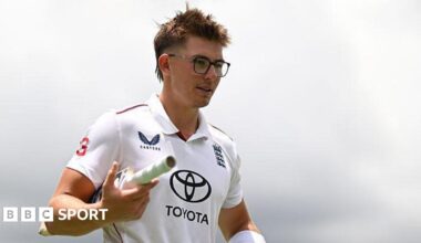 Asa Tribe of the England Lions walking off the field with a bat tucked in between his right arm.