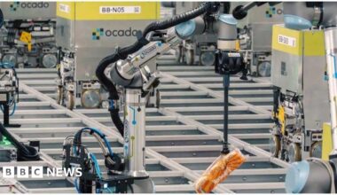 A series of silver robots move around on rails. In the foreground, one picks up Warburton crumpets with an arm