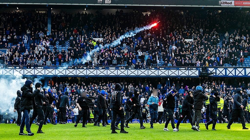 A flare or firework flies through the air as fans invade the pitch at Ibrox after the Old Firm match on Sunday, March 8.