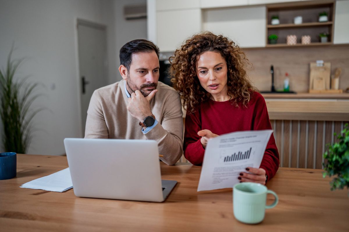 Couple reviewing financial documents and using laptop at home. Planning budget and managing expenses together
