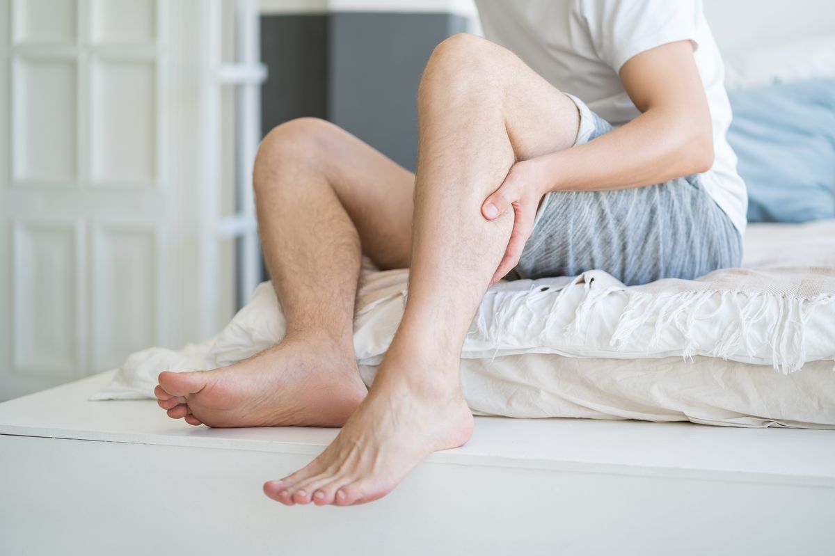 The man's calf muscle cramped, massage of male leg at home, painful area highlighted in red