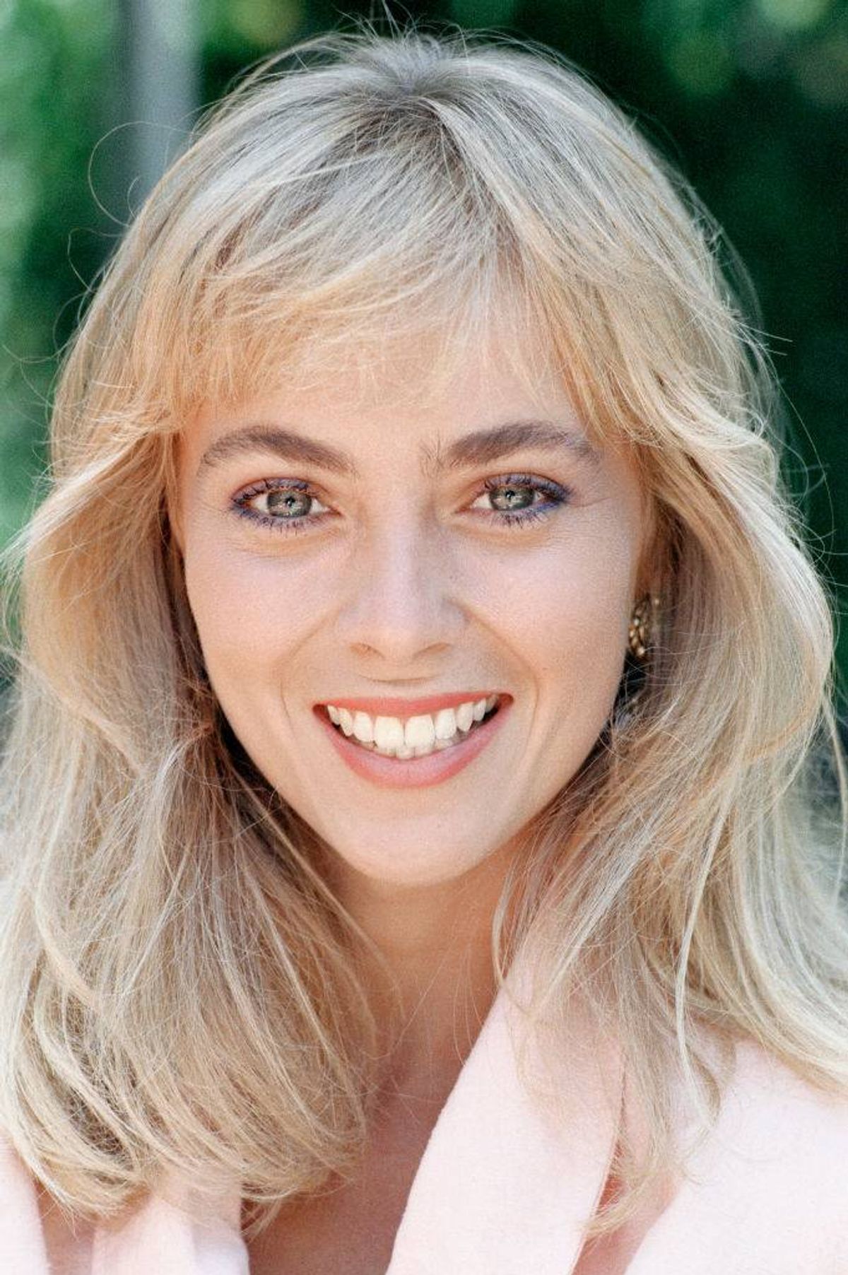An individual with light blonde hair and a cheerful expression, showcasing a radiant smile. The individual is gazing directly at the camera, with natural light enhancing their features.