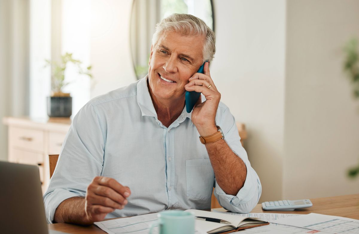 Happy elderly man with phone call, laptop or communication for home budget, consulting financial advisor or planning savings in living room. Investment or insurance with mobile or smartphone admin
