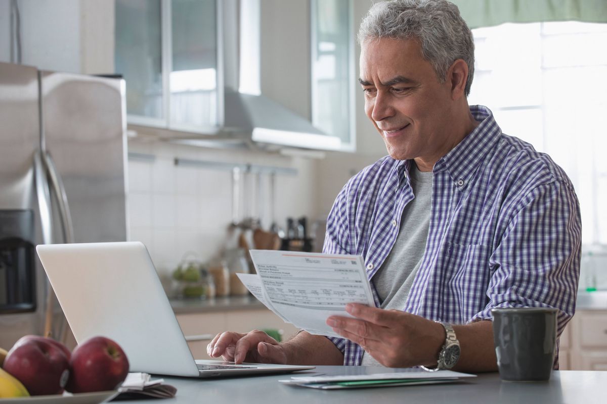 Hispanic man paying bills online in kitchen