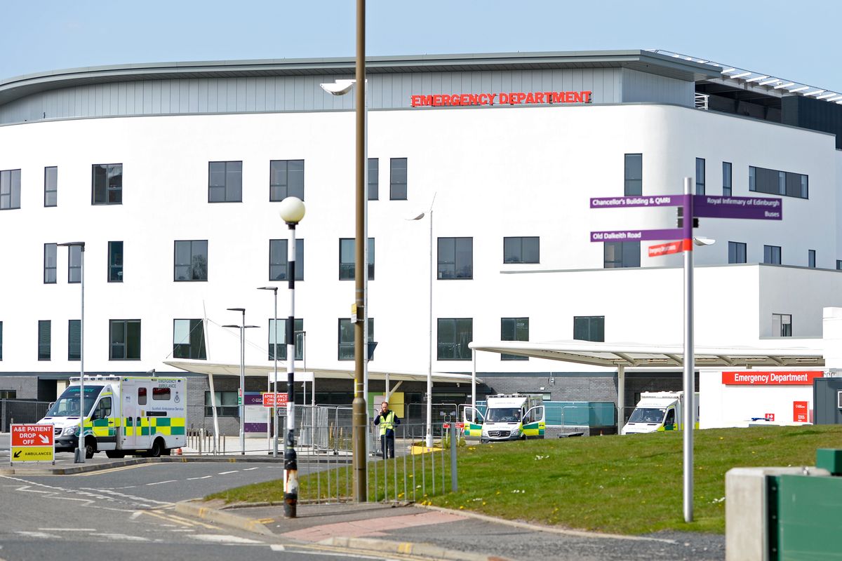 An image of the exterior of a modern white hospital building with ambulances outside.