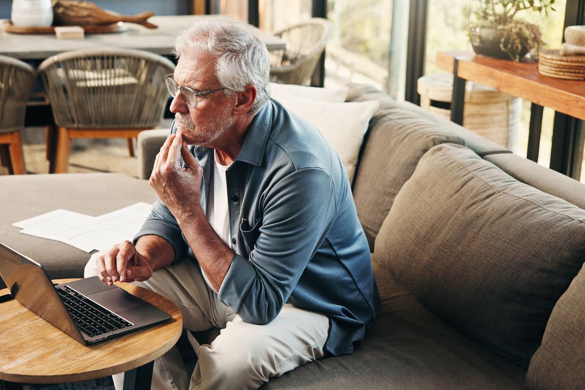 Old man, thinking and reading in home with laptop for asset management, retirement fund or prepare will. Senior person, reflection or browse on sofa with computer, pension annuity or estate planning.