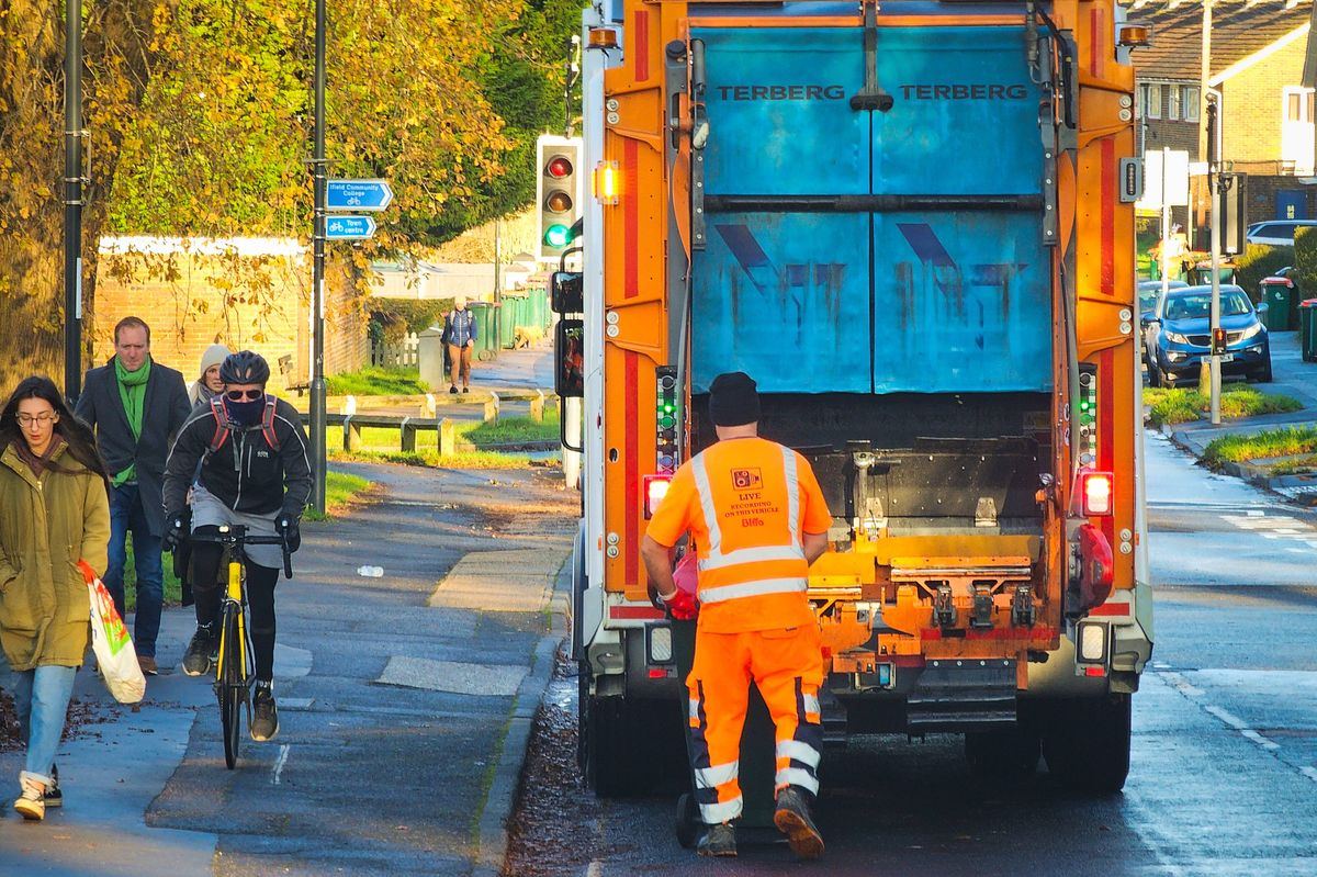 Crawley, UK - 26 November, 2024: color image depicting one refuse collection worker, wearing reflective workwear, emptying a garbage bin into the garbage truck on a city street in Crawley, West Sussex, in southeast England.