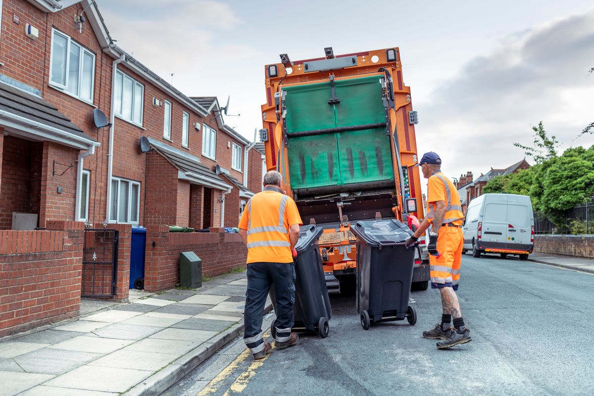 Refuse collectors with bins and refuse truck in street