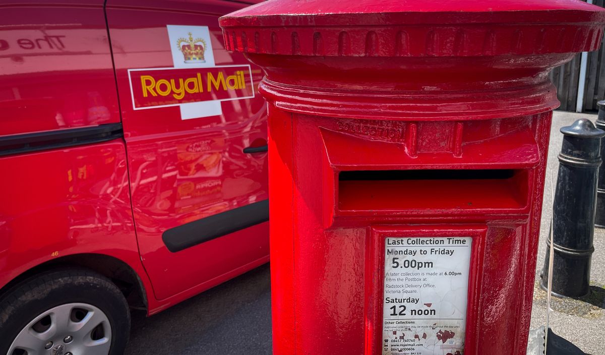A Royal Mail van waits beside an original red post box as its driver collects post left at a branch of the Post Office