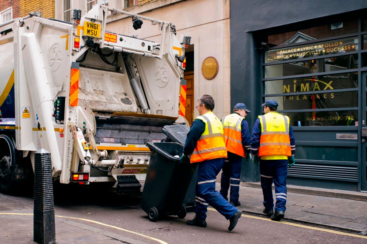 London, England - March 28, 2015: A crew of refuse collectors working in Maiden Lane in Central London, taking containers of rubbish to the lorry for loading. They are wearing bright yellow and orange hi-visability jackets to help them avoid accidental injury in London’s busy streets.