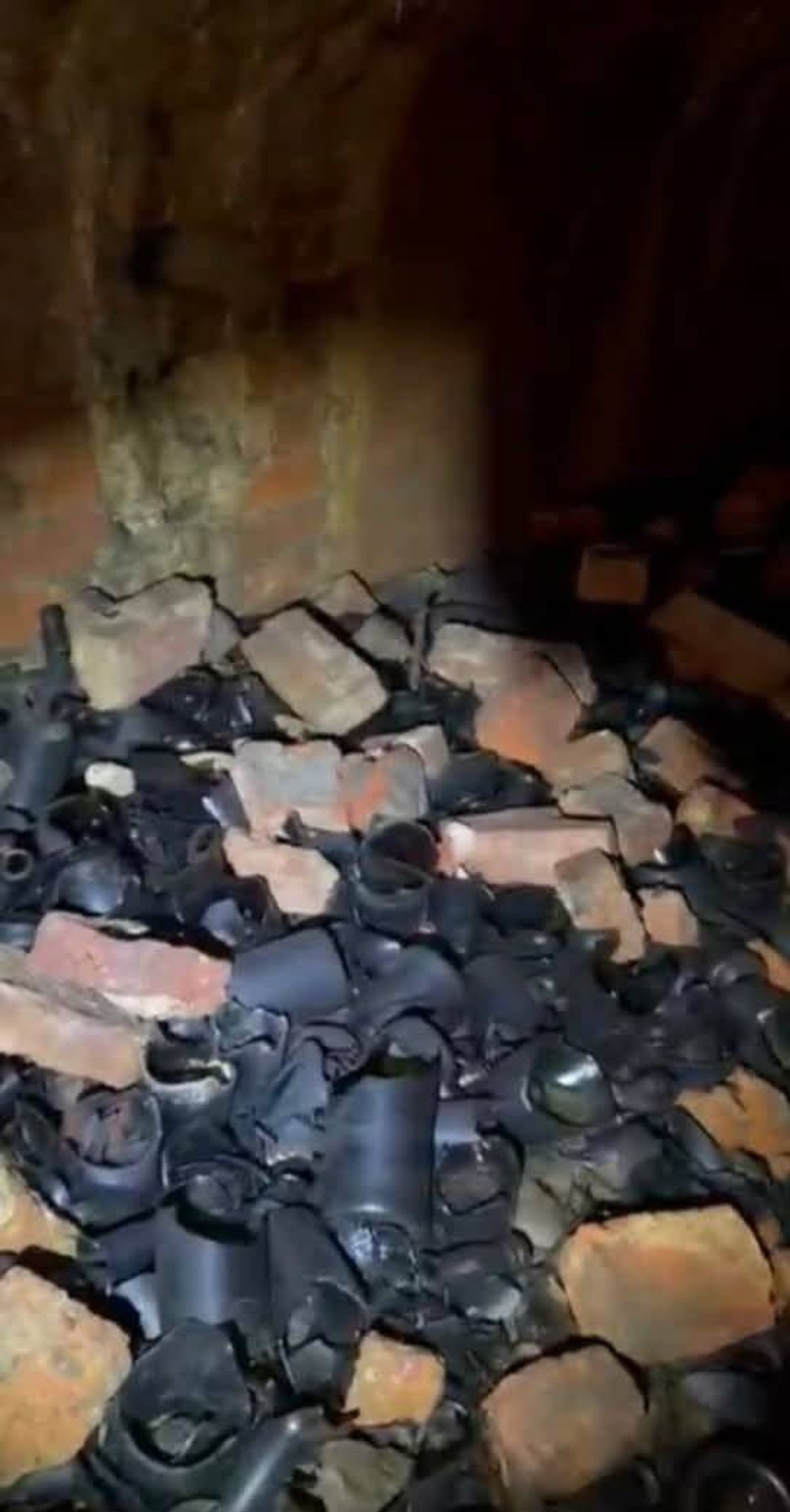 A dimly lit area showing a collection of discarded materials, including various black pipes and reddish bricks, possibly from a demolished structure.