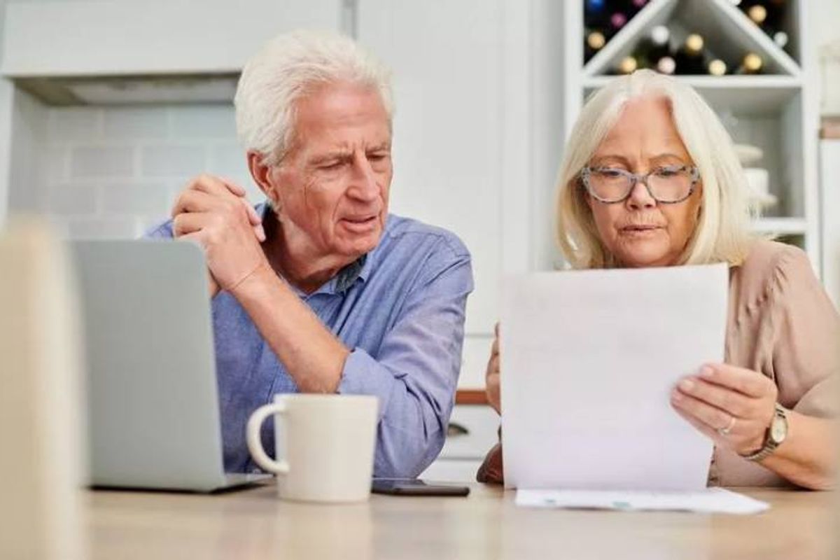 An older man and woman are seated reading a letter. 