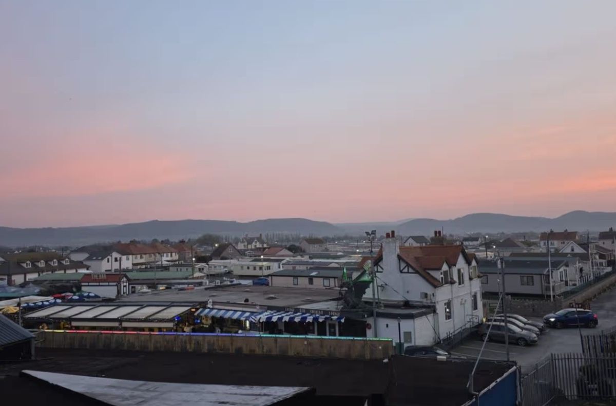 The image shows a view of caravans and rooftops beside the sea at dusk