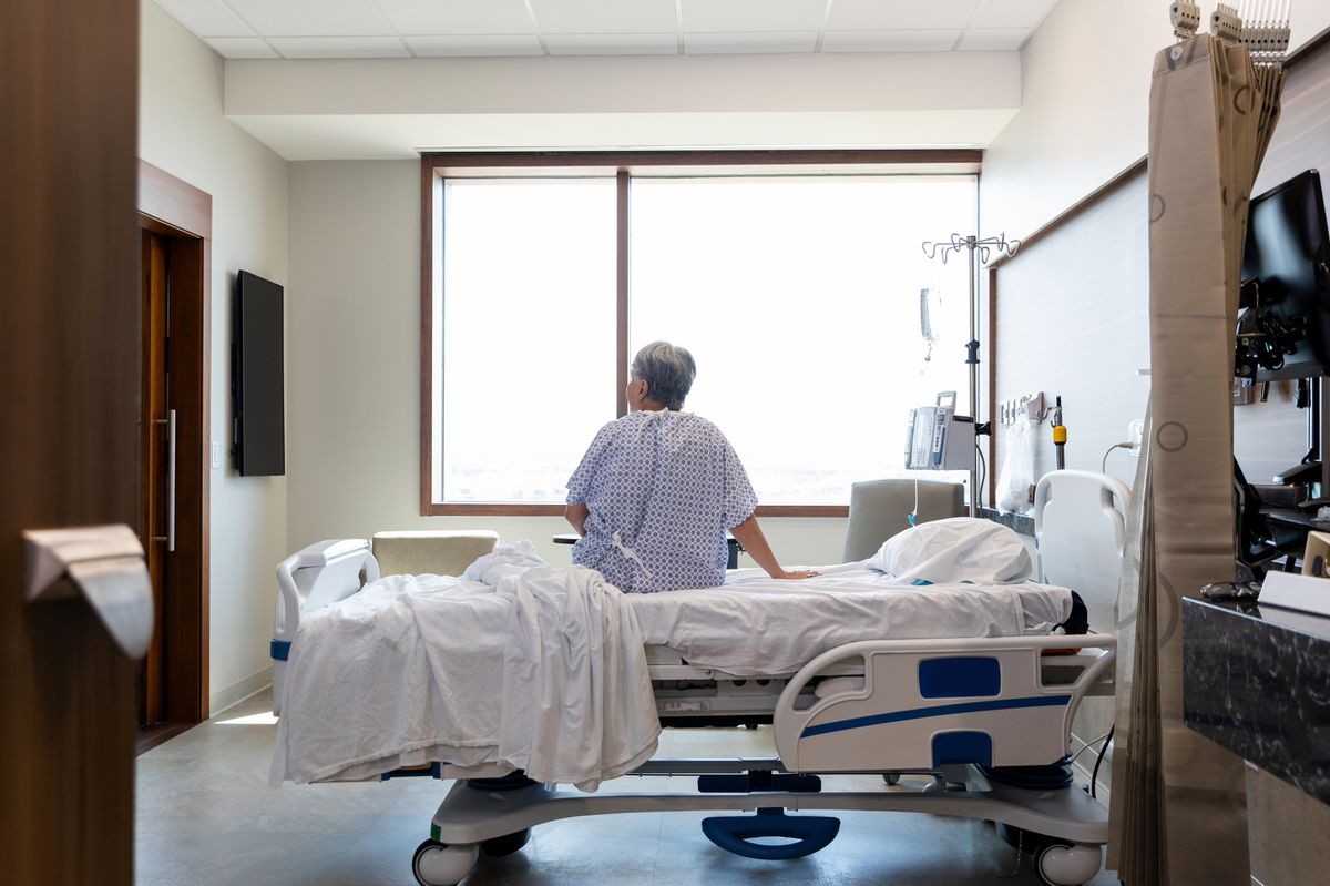 The senior adult woman sits alone in her hospital room while she waits for her daughter.