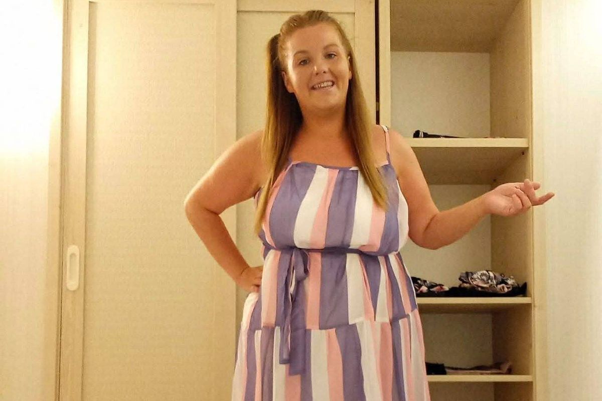 Woman standing in front of wardrobe wearing a sleeveless dress with purple and pink stripes