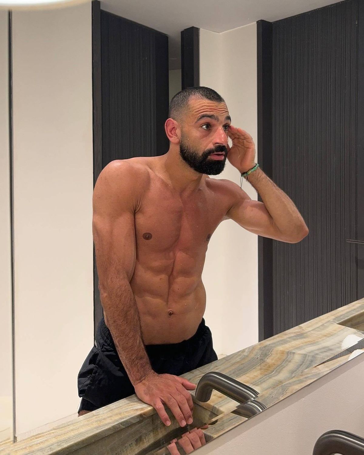 Mohamed Salah, with his shirt off, looking into a bathroom mirror in his home