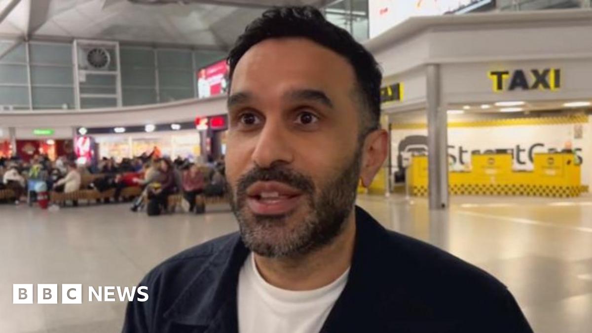 People with suitcases are hugged by loved ones in Stansted Airport's arrivals lounge, with the arrivals board visible behind them.