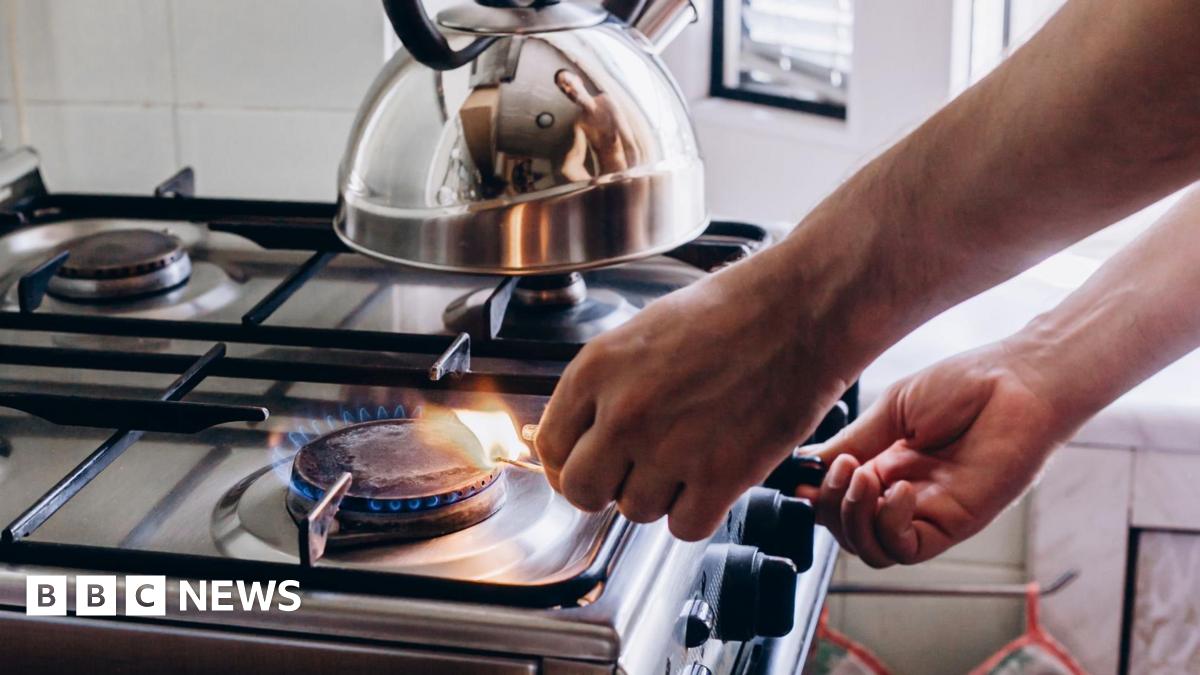 A person lights a gas stove using a match. There is a silver kettle sitting on one of the rings.