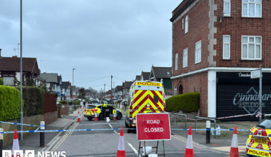 A woman with dark hair and a multiple colour jumper siting on a green sofa inside her living room.