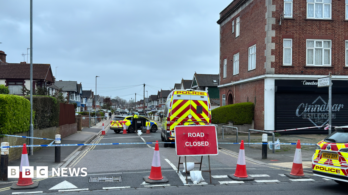A woman with dark hair and a multiple colour jumper siting on a green sofa inside her living room.