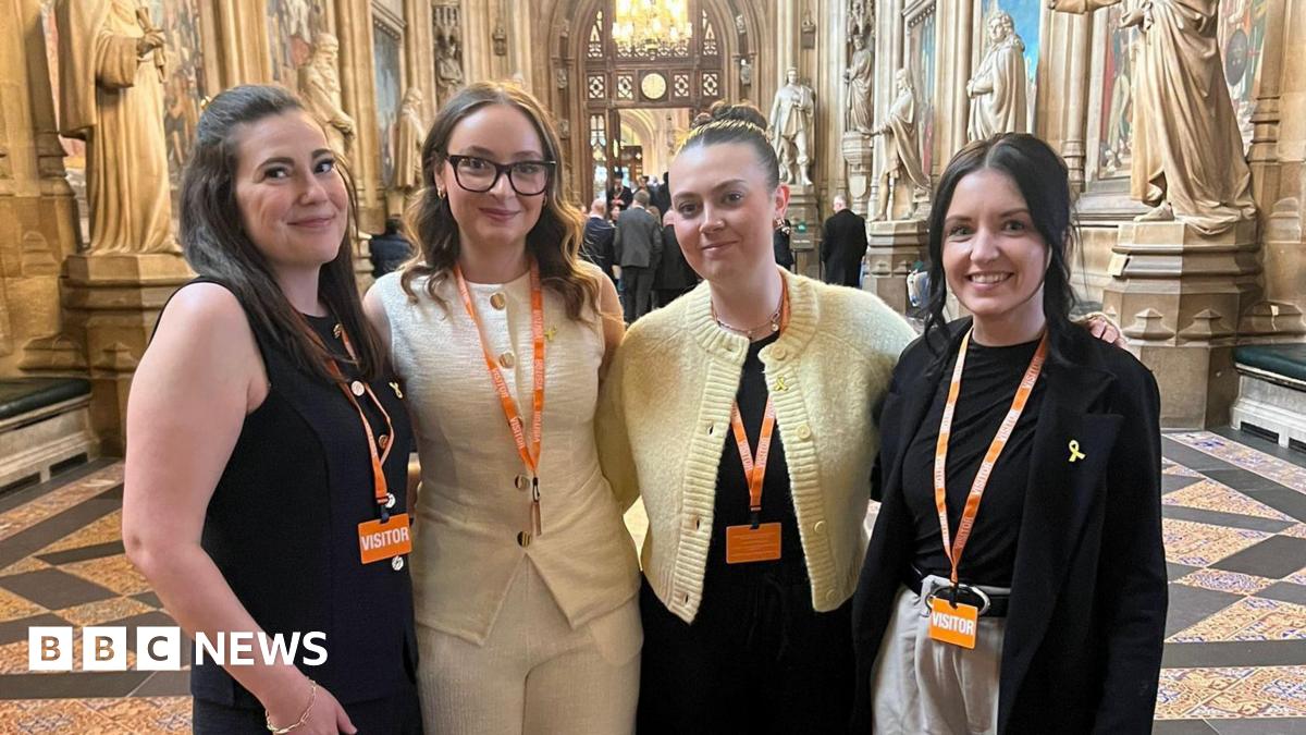 Four women stand in Westminster together smiling at the camera. They are dressed smart and have orange lanyards around their necks.