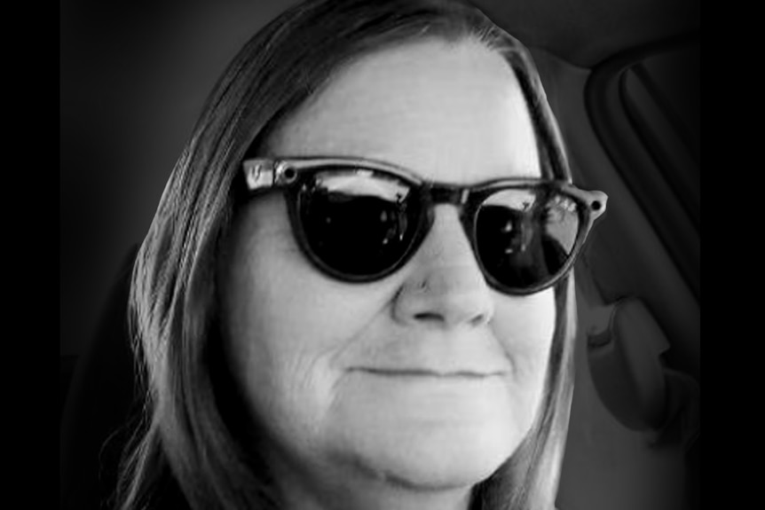 A woman with shoulder-length, dark hair wearing dark sunglasses and grinning.