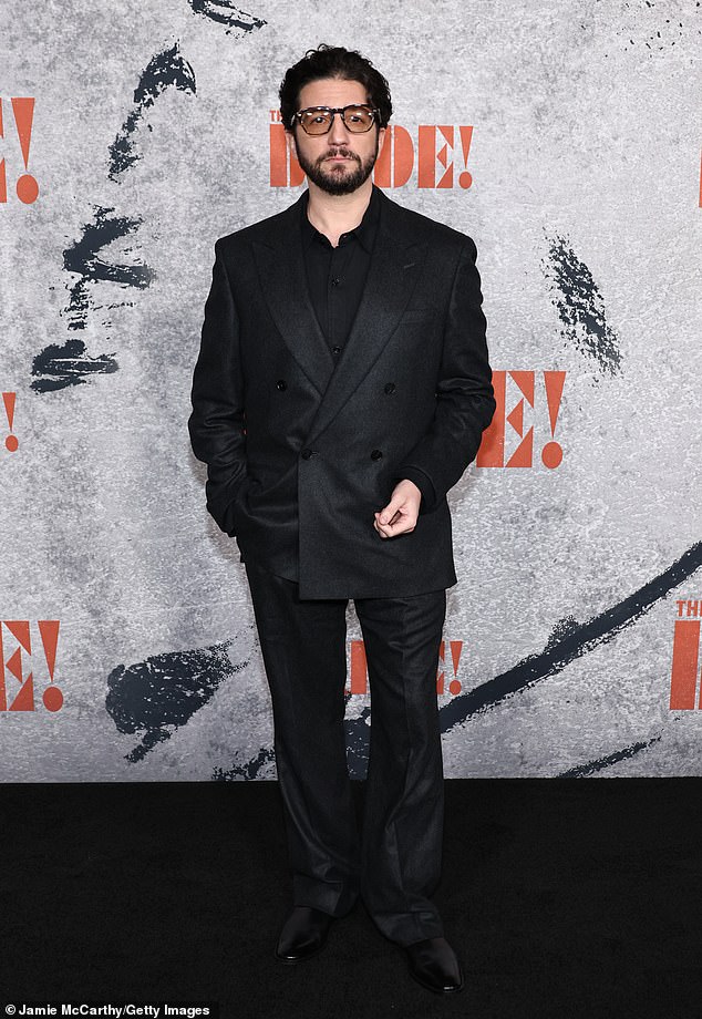 Materialists actor John Magaro - who plays a mystery role in The Bride - rocked yellow-lensed sunglasses with his black double-breasted suit and patent leather Oxfords