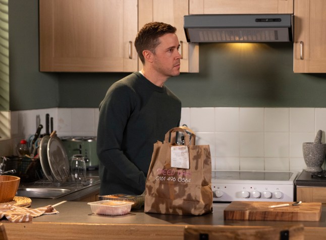 Todd Grimshaw looking sad in his kitchen in Coronation Street, next to a takeaway bag from Speed Daal.