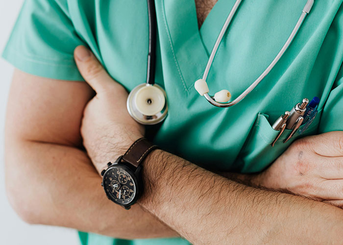 Doctor in green medical scrubs with stethoscope and watch, arms crossed illustrating medical secrets concept.